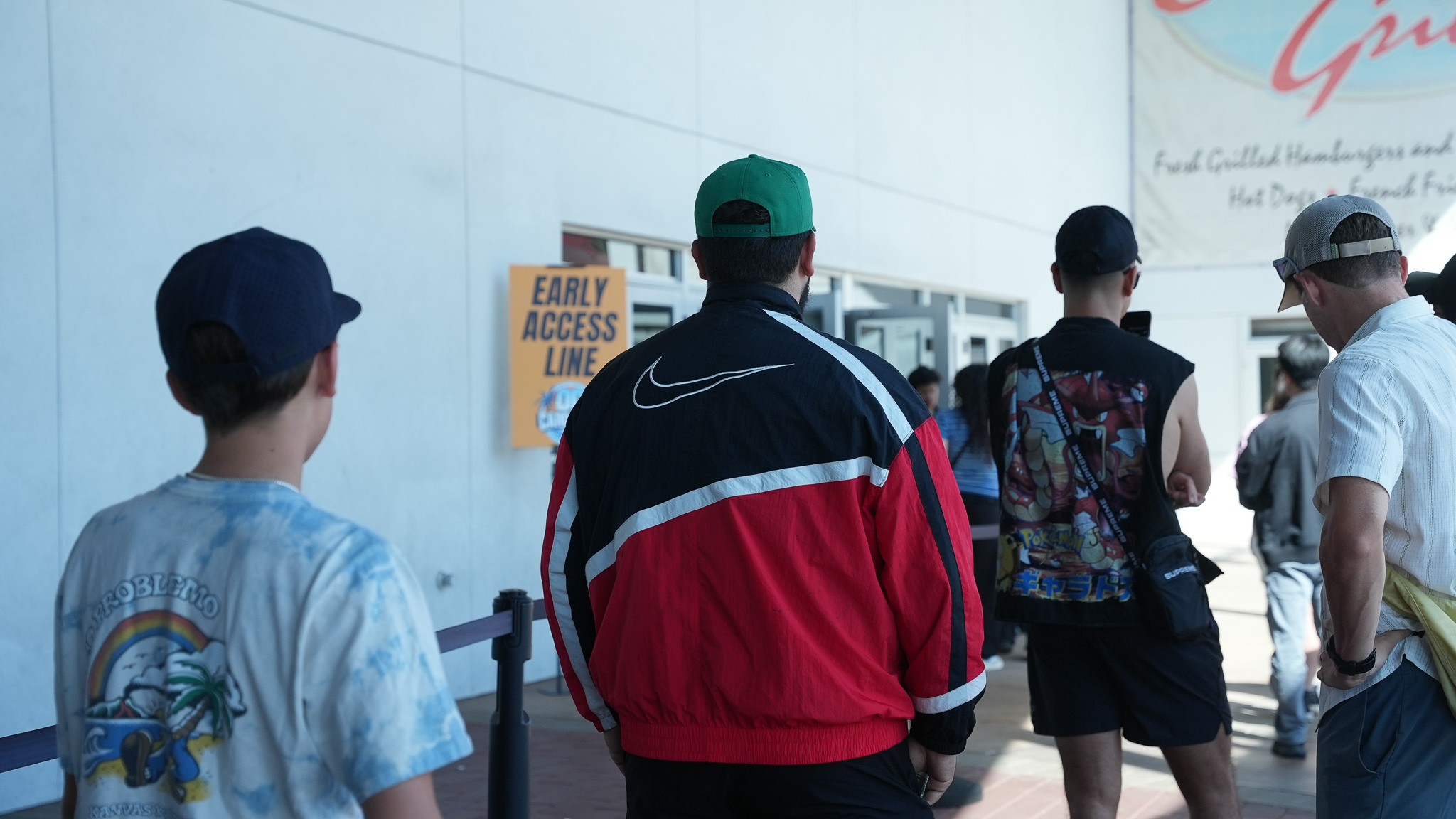 Attendees waiting in the early access line outside a show entrance, several wearing vintage windbreakers and Pokémon-themed apparel