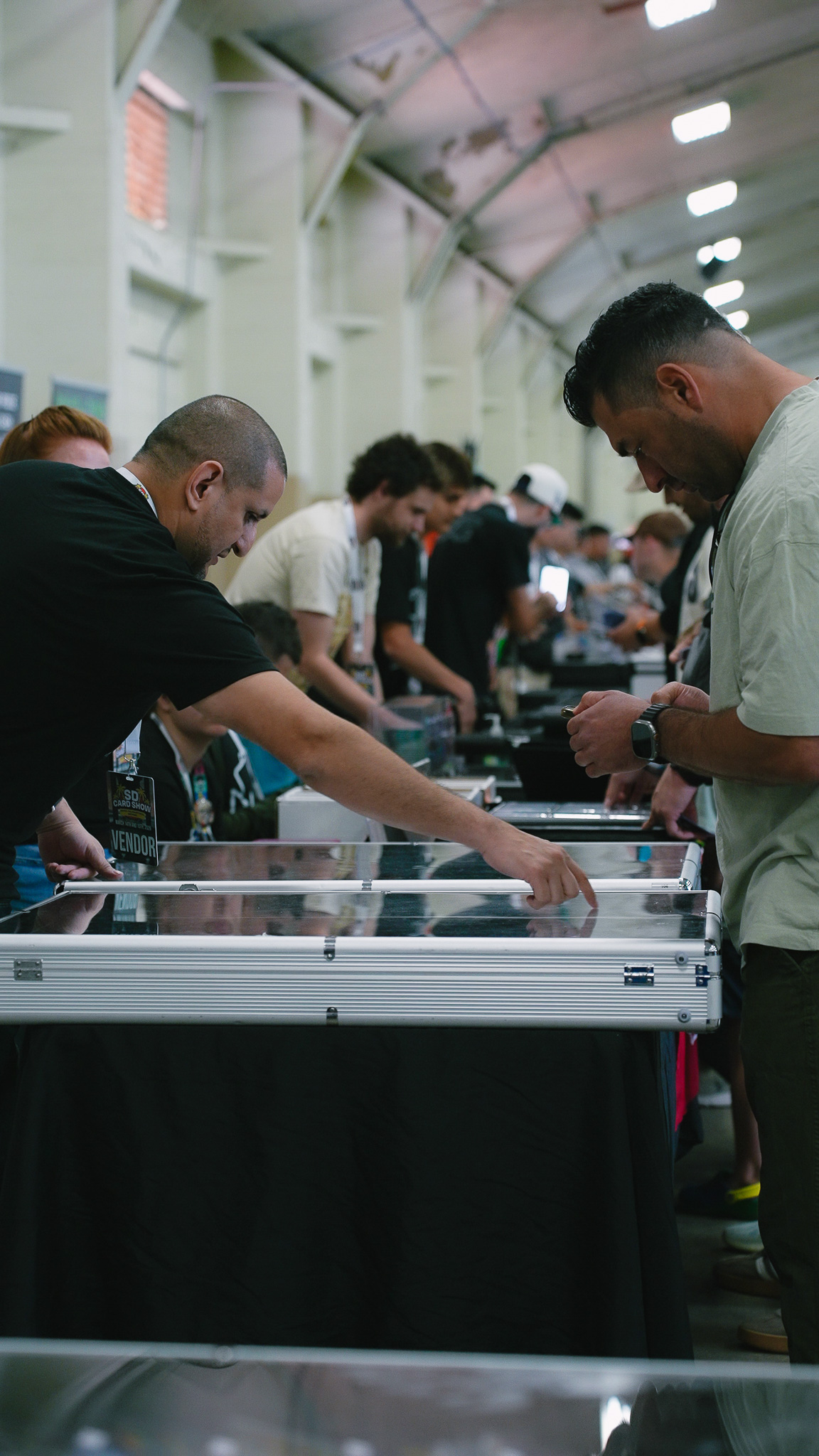 Vendor pointing out a card in a glass display case to a customer at his booth
