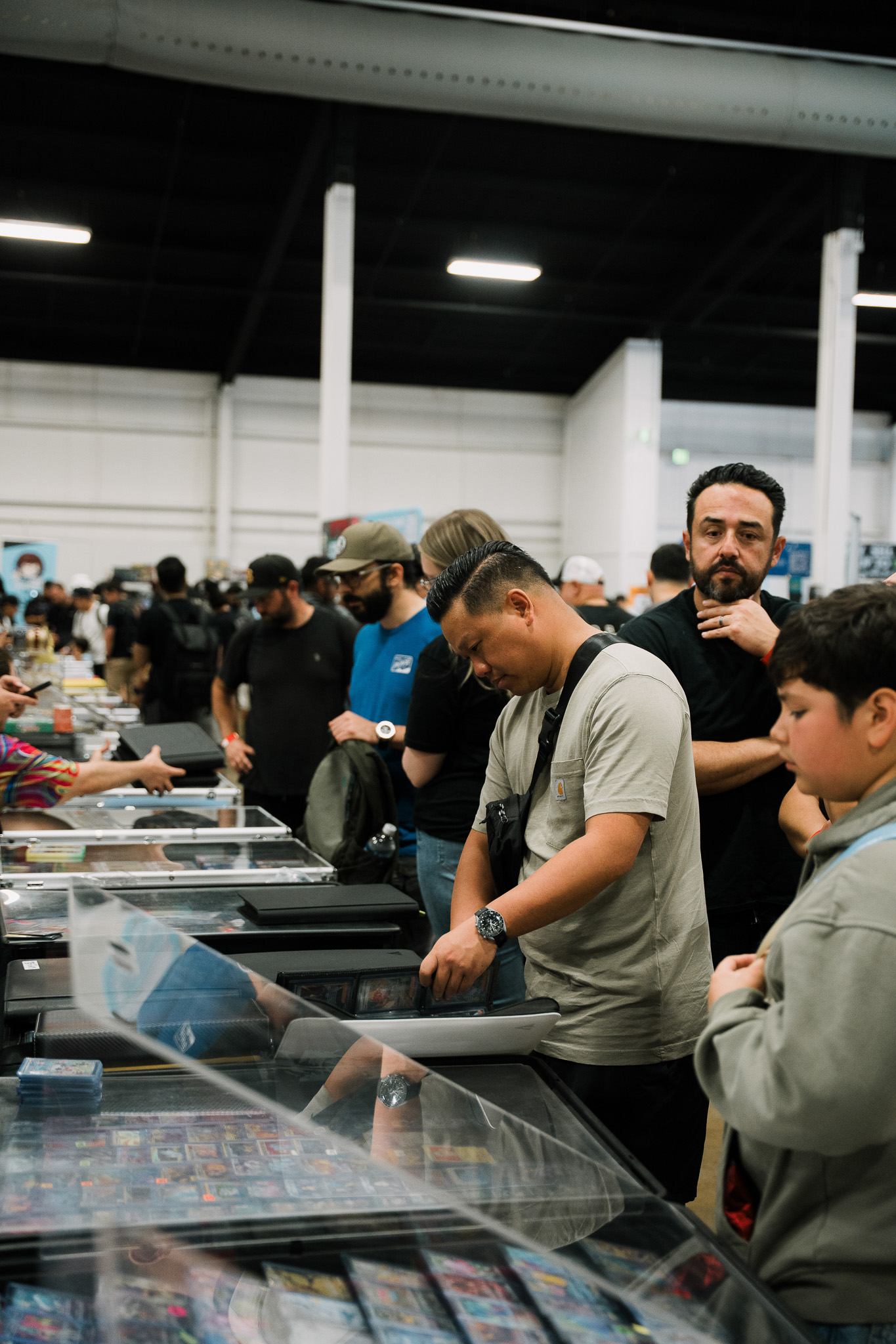 Crowd of collectors browsing display cases of graded trading cards along a row of vendor tables