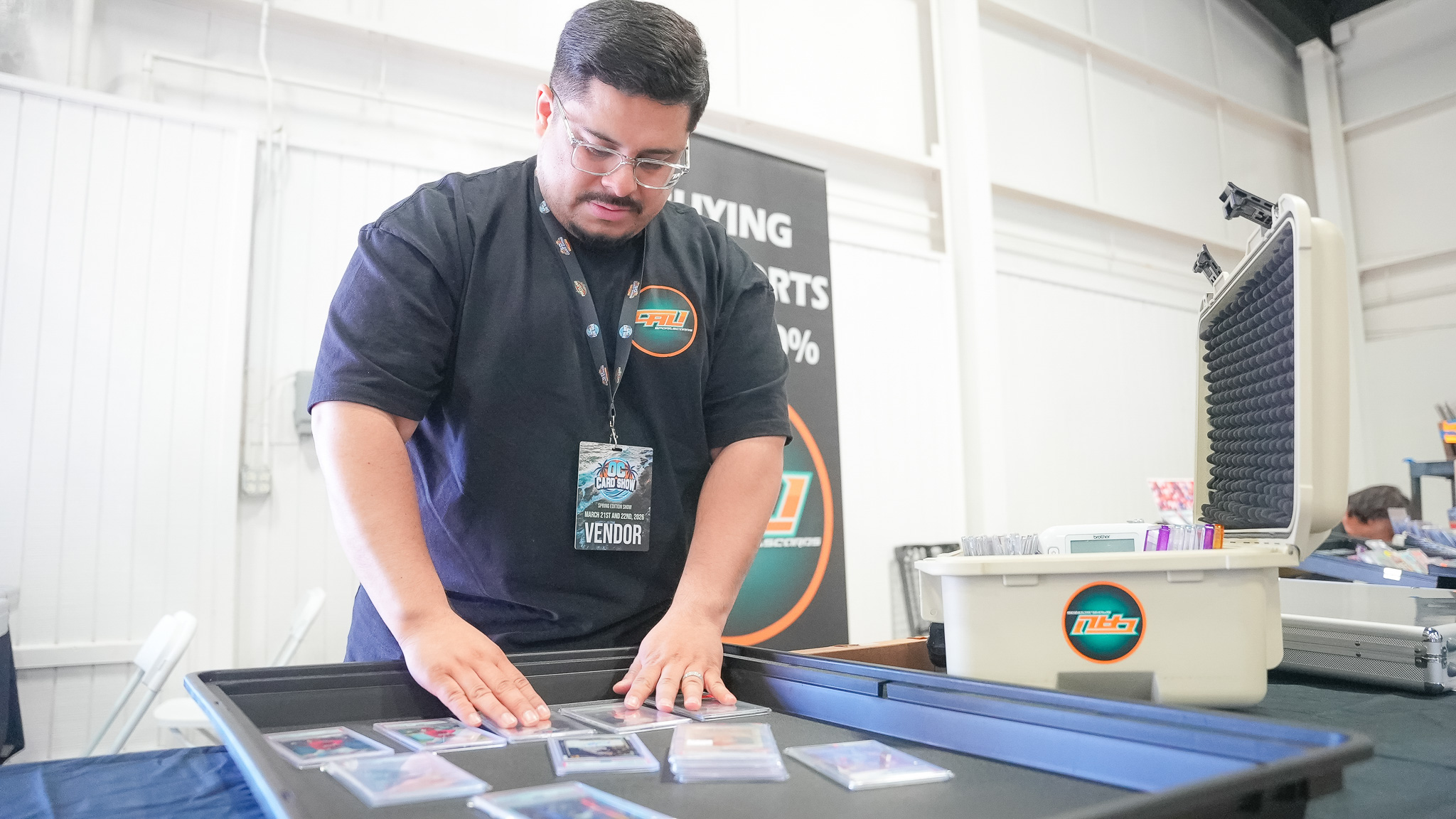 Vendor wearing a show badge arranging graded trading cards on a display tray at his booth