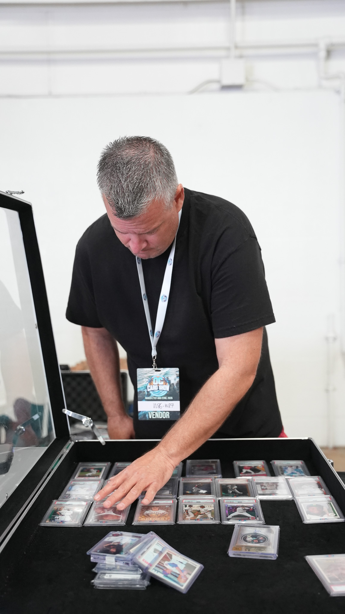 Vendor reaching into an open display case of graded baseball cards at his booth