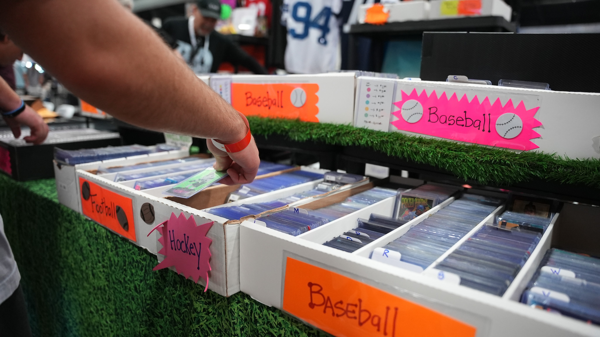 Hand sorting through trading cards in bins labeled Baseball, Football, and Hockey