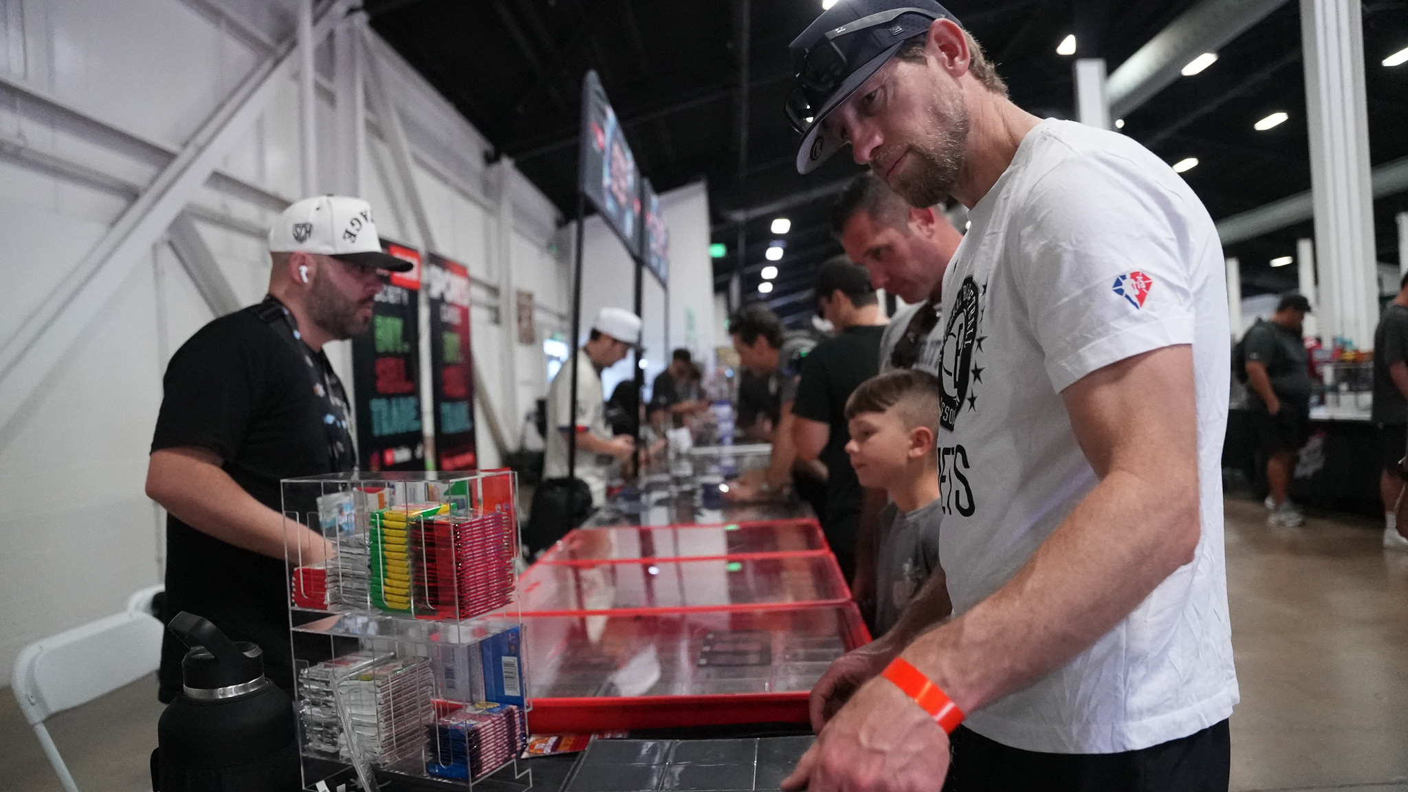 Collectors browsing a glass display case filled with trading cards at a vendor table